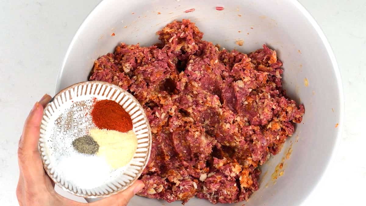 adding spices and seasoning to bowl of meatball mix
