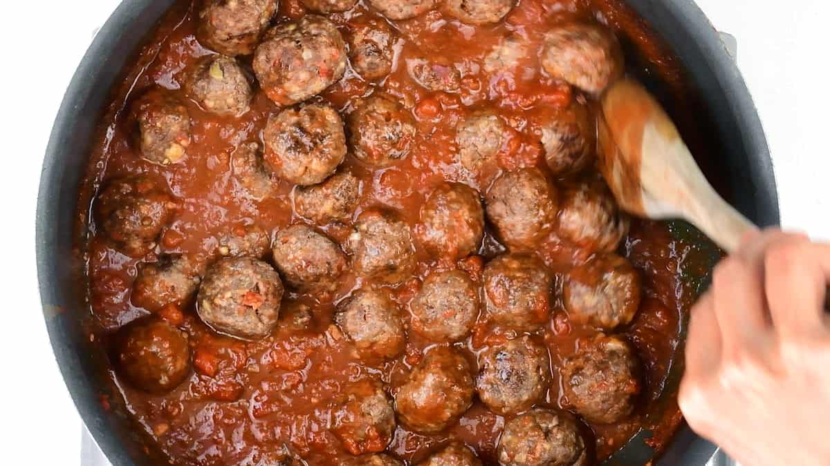 stirring Spanish meatballs in tomato sauce in a pan