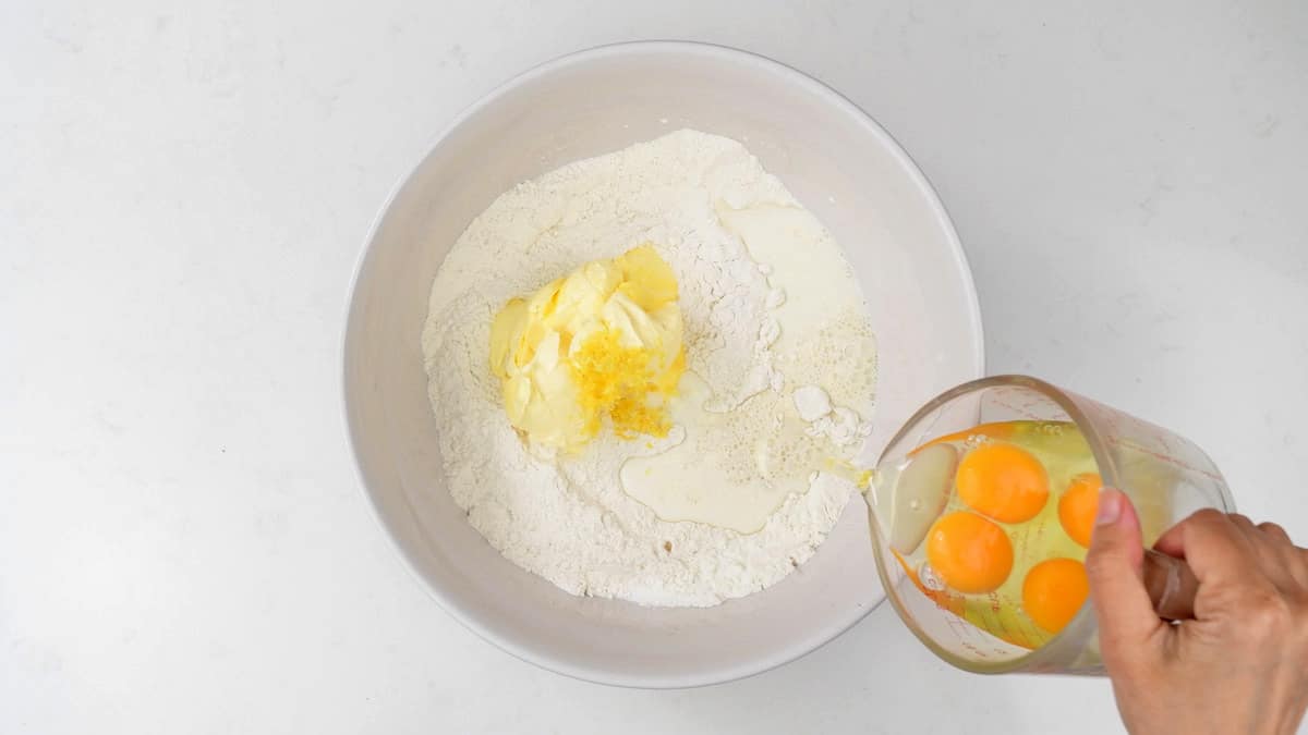 Adding eggs to a mixing bowl with flour, sugar, butter and milk