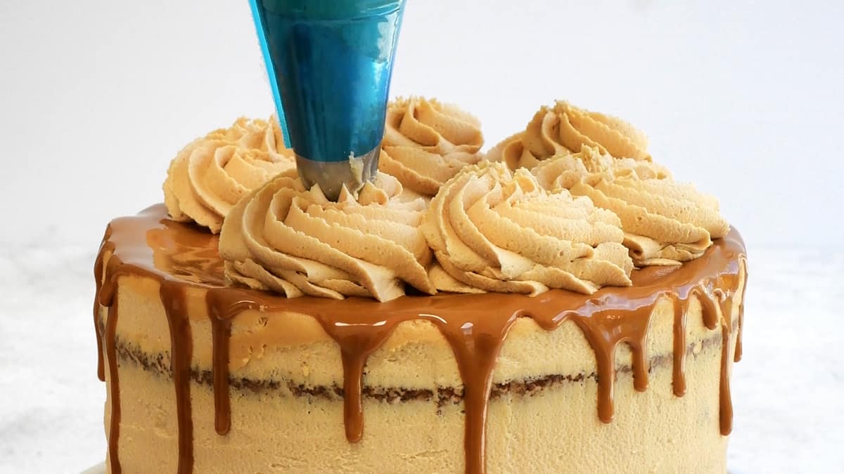 piping Biscoff buttercream over cookie butter cake