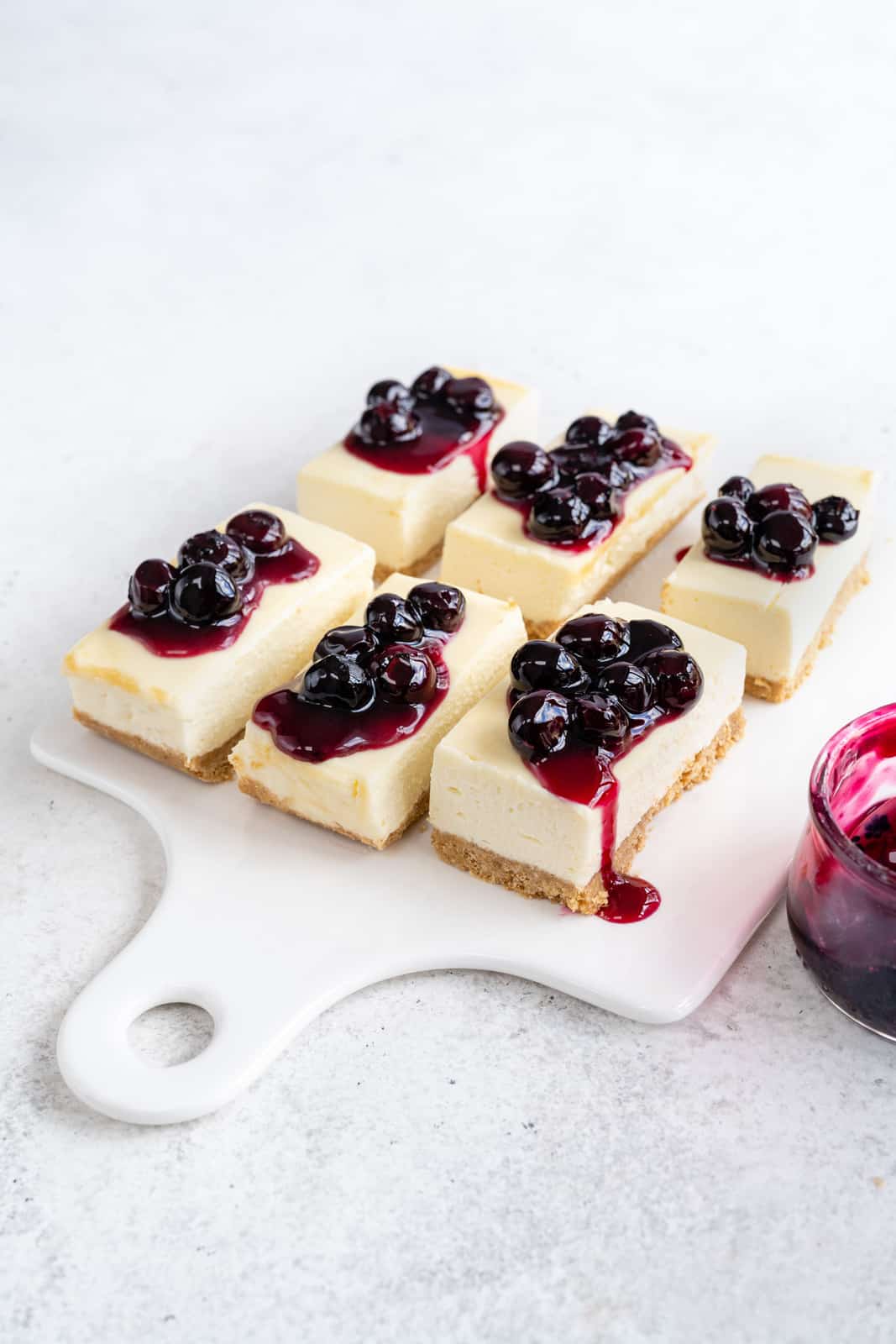 No Bake Cheesecake bars topped with blueberry compote on a white board