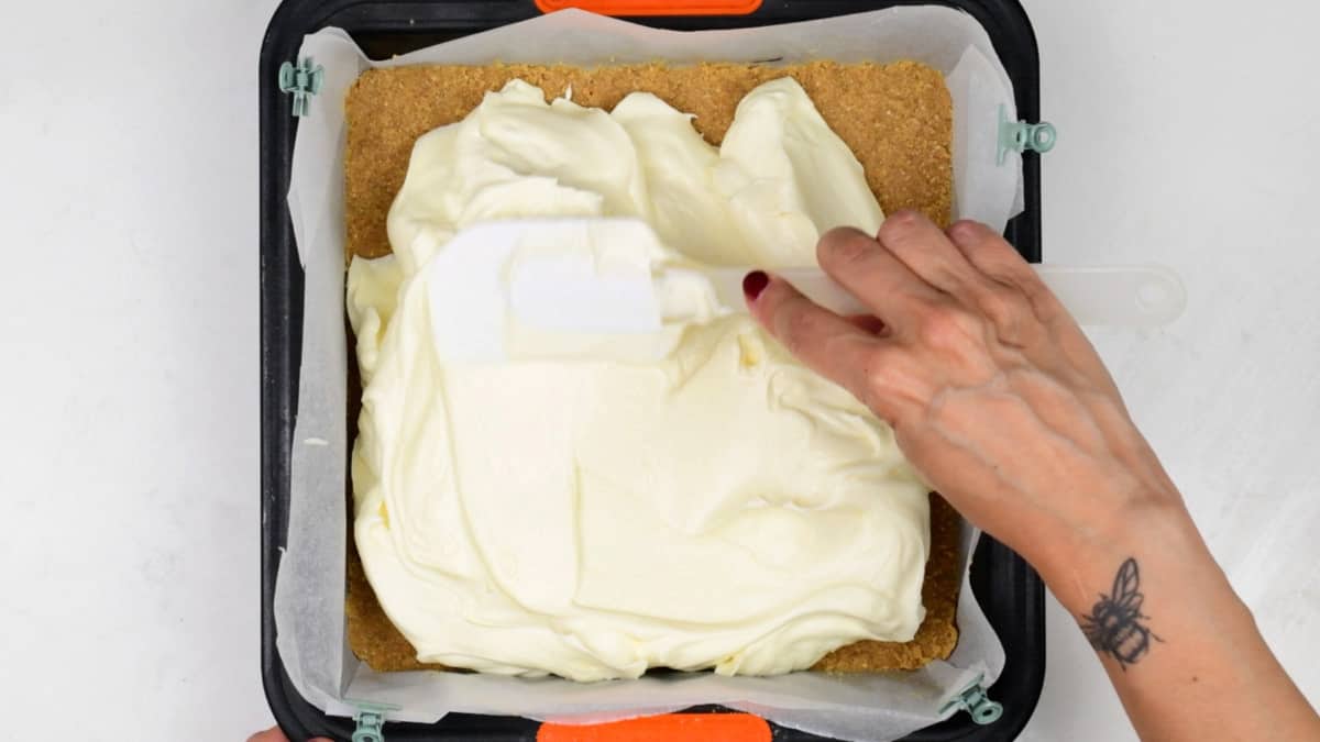 spreading cheesecake filling over chilled base in a square tin