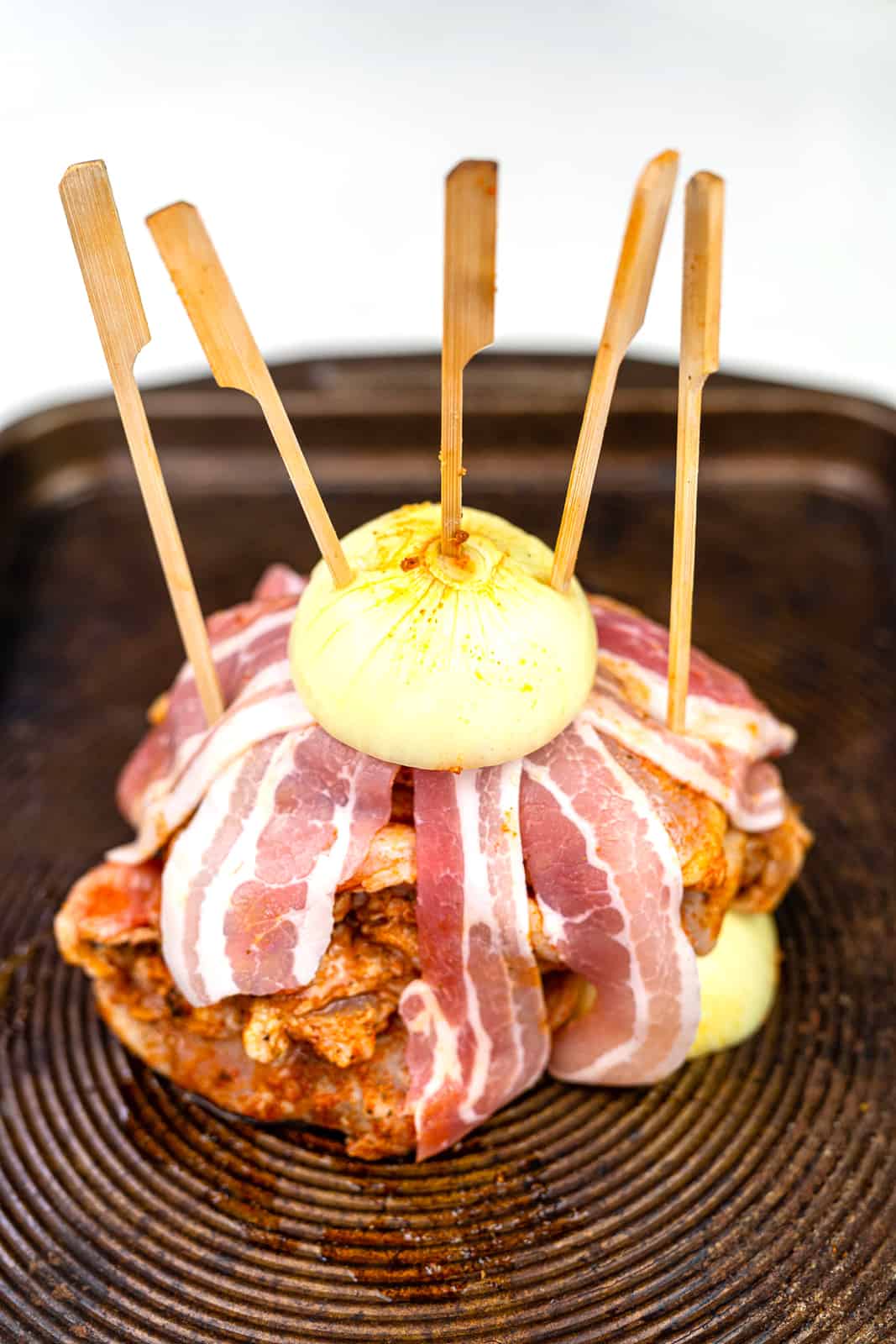 Marinated chicken in a stack topped with streaky bacon and half an onion, secured by wooden skewers