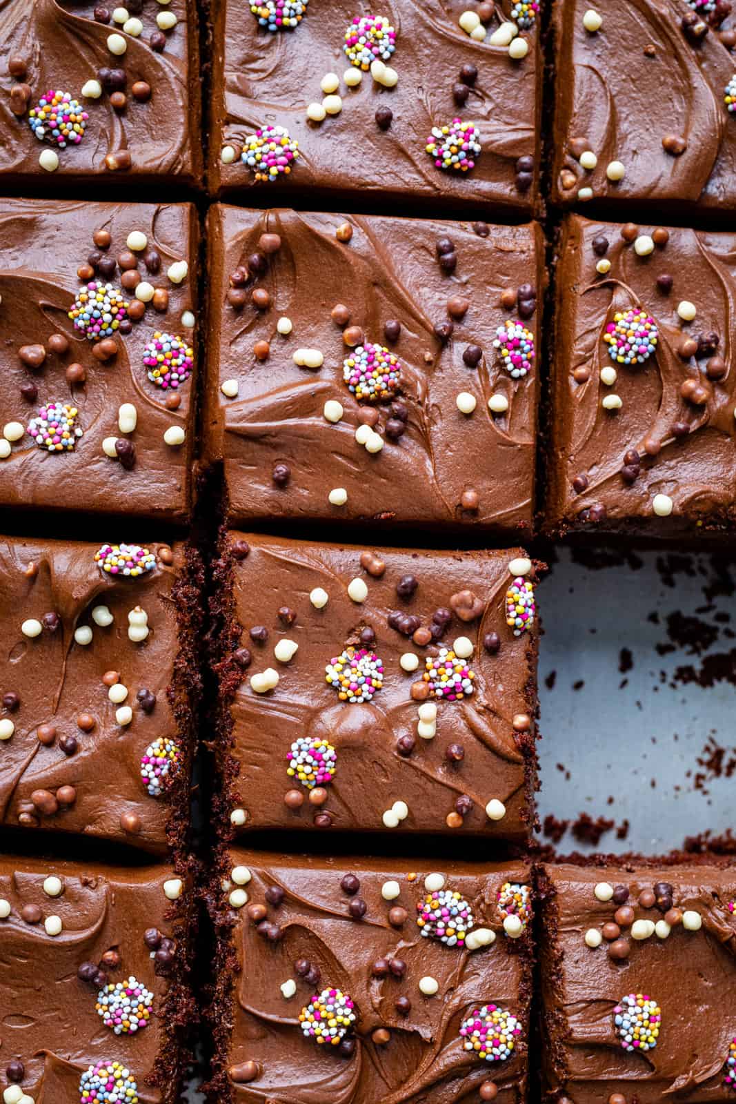 close up on a chocolate traybake covered in chocolate frosting and sprinkles and cut into squares