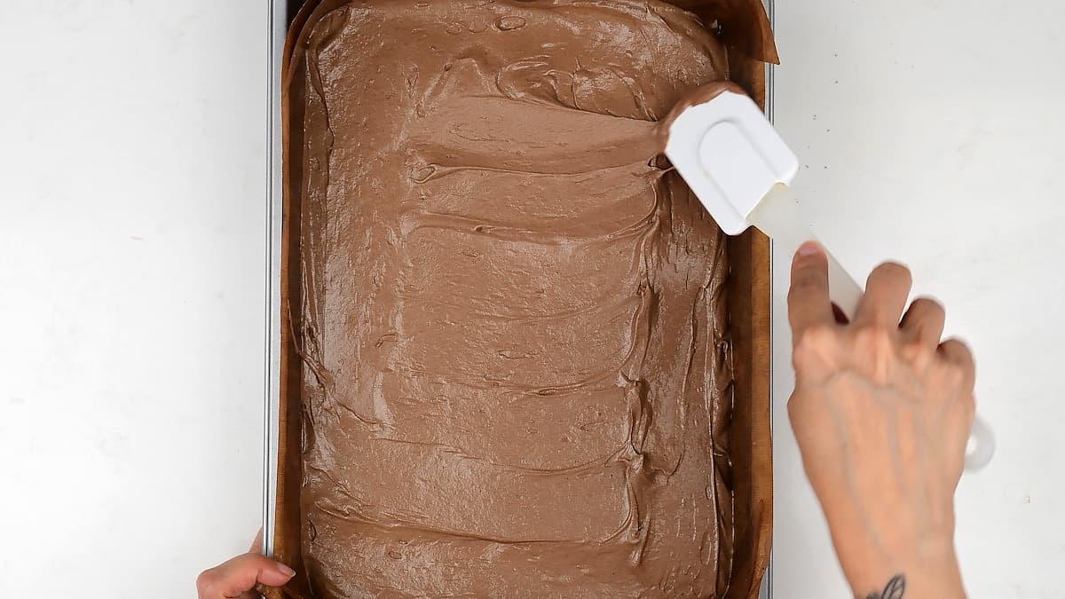 spreading chocolate cake batter in a rectangular baking tin