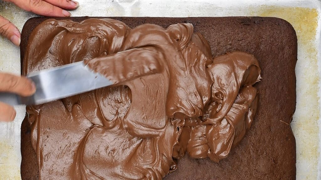 spreading chocolate frosting over a chocolate cake traybake