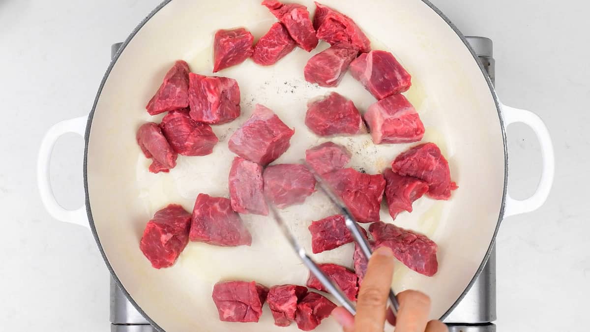 browning beef cubes in a shallow cast iron casserole