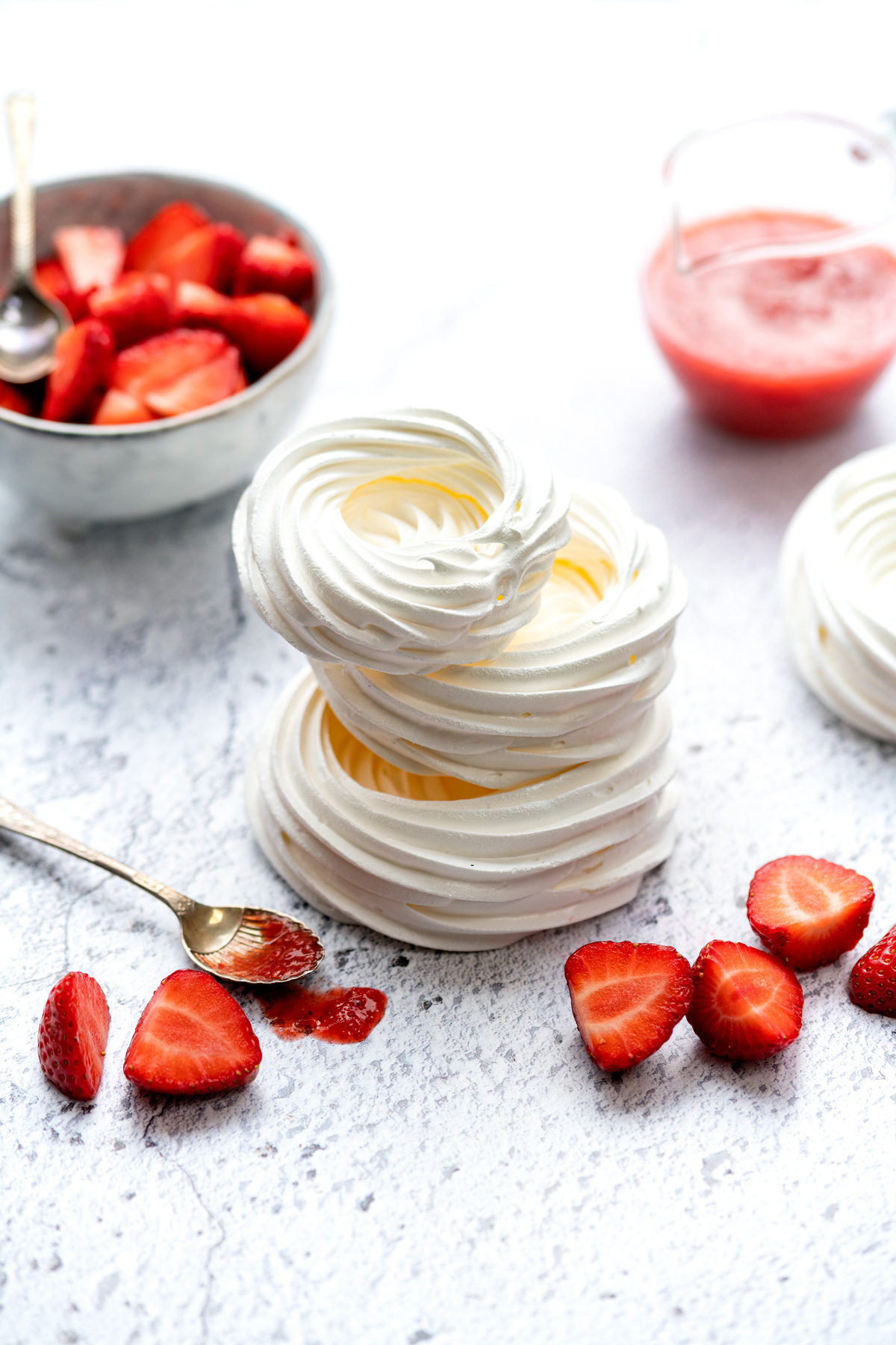 Three meringue nests stacked with a bowl of sliced strawberries on the side
