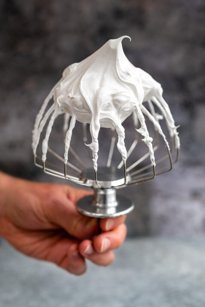Swiss meringue holding firm peaks on a whisk