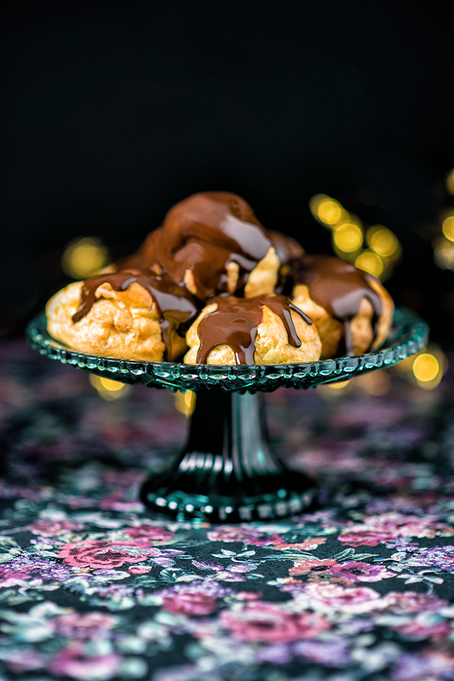 Pile of profiteroles on a cake stand covered with chocolate sauce