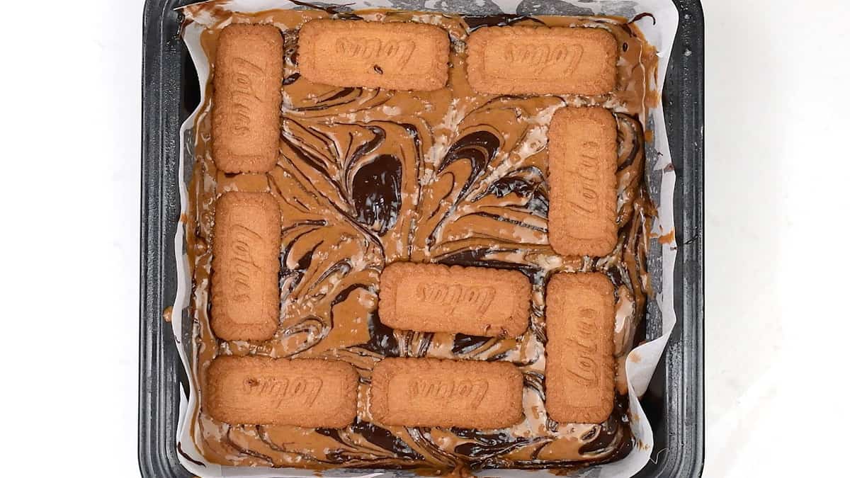 Placing Biscoff biscuits on brownie batter in a square tin