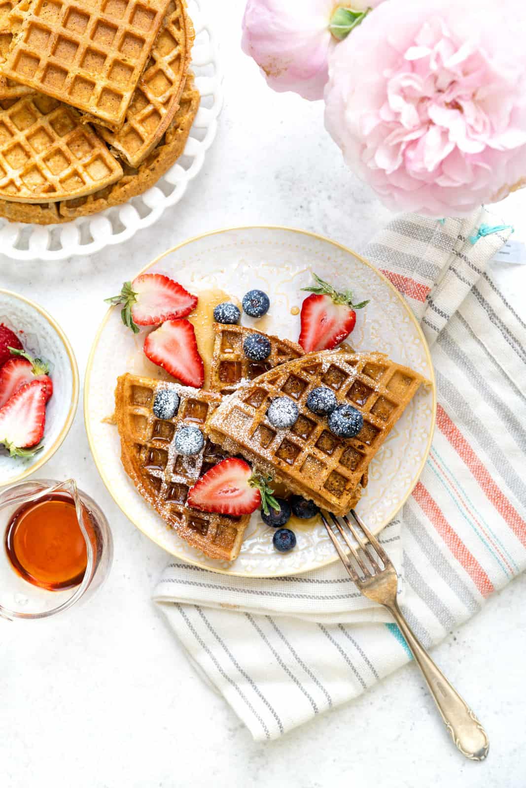 Table set with plates of healthy oat waffles with fresh berries and maple syrup