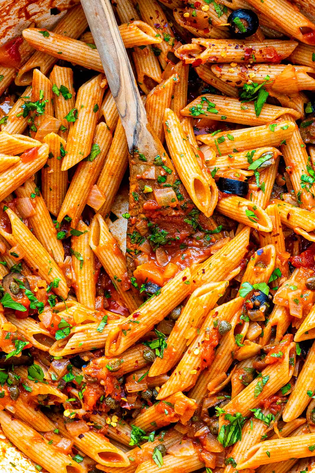 Close up on pan of Penne Puttanesca with olives, capers and anchovies