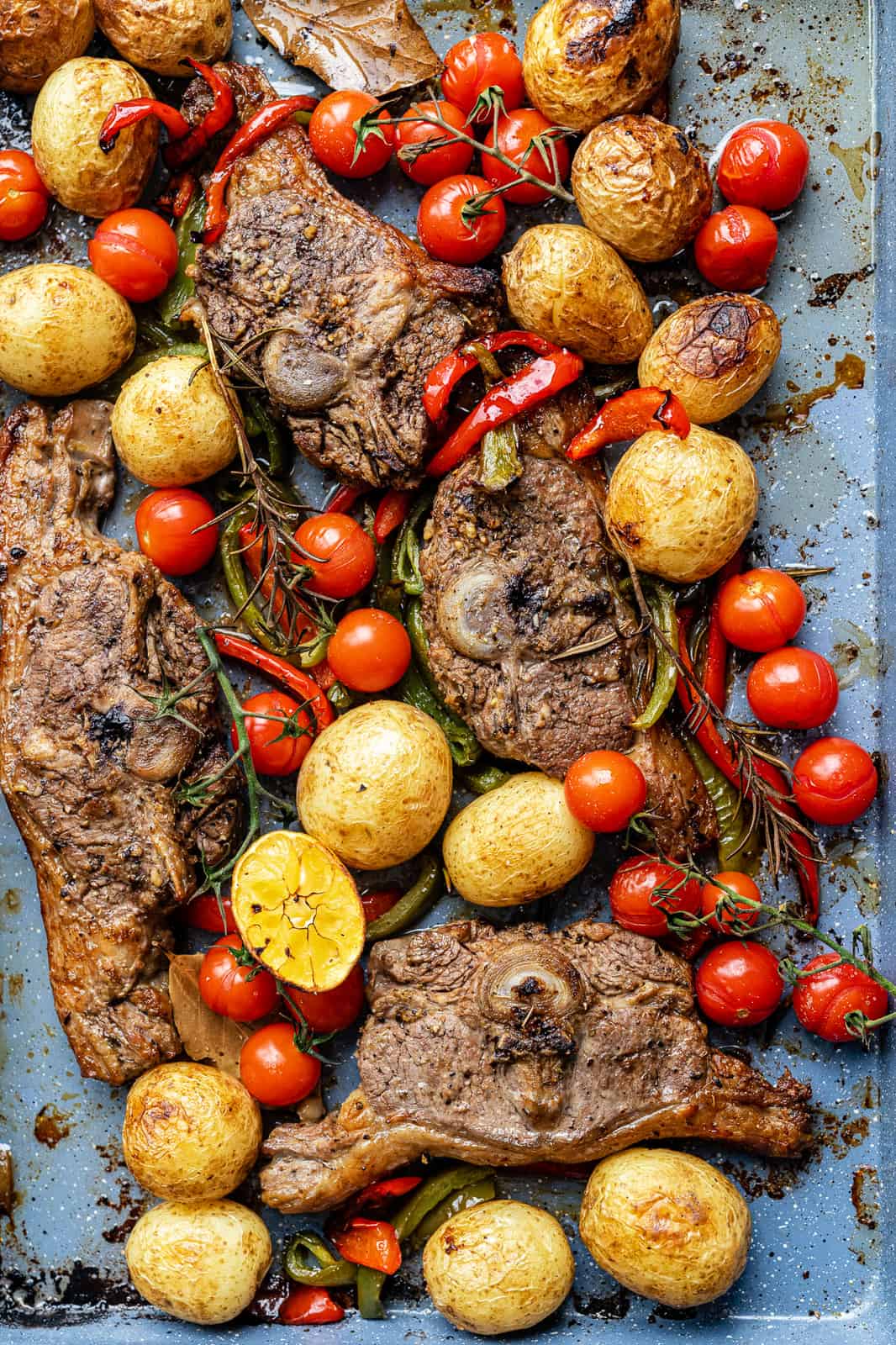 close up on a roasting tin with roasted lamb chops, potatoes, tomatoes and peppers