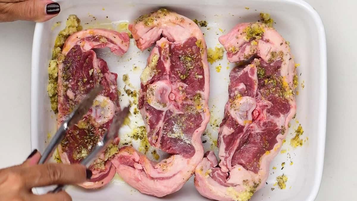 mixing marinade over thick lamb chops in a ceramic dish