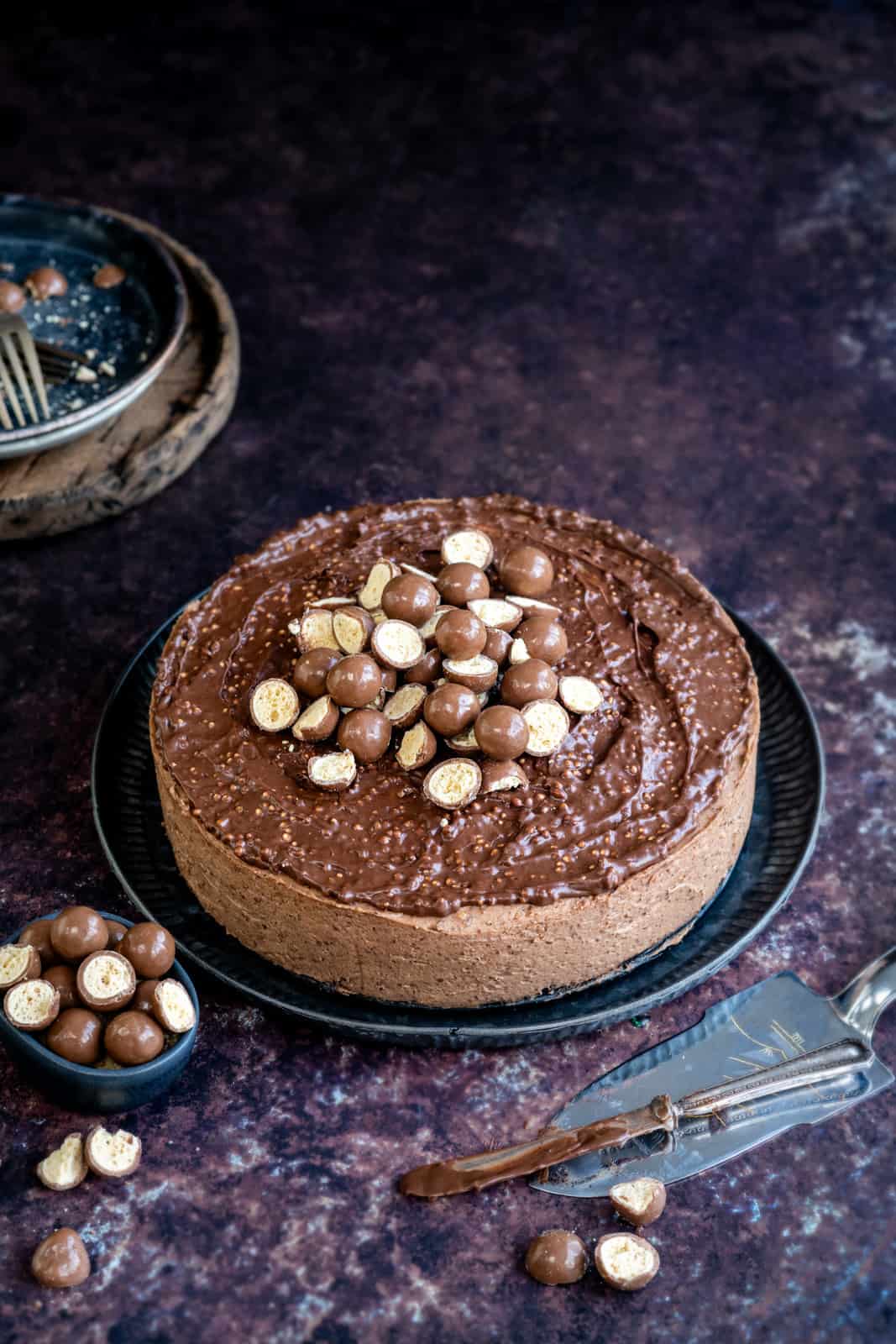 Maltesers No Bake Cheesecake on a plate decorated with chopped Maltesers and Malteser Chocolate spread