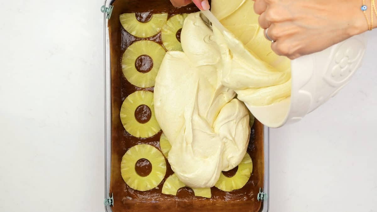spreading cake batter over pineapple in cake tin