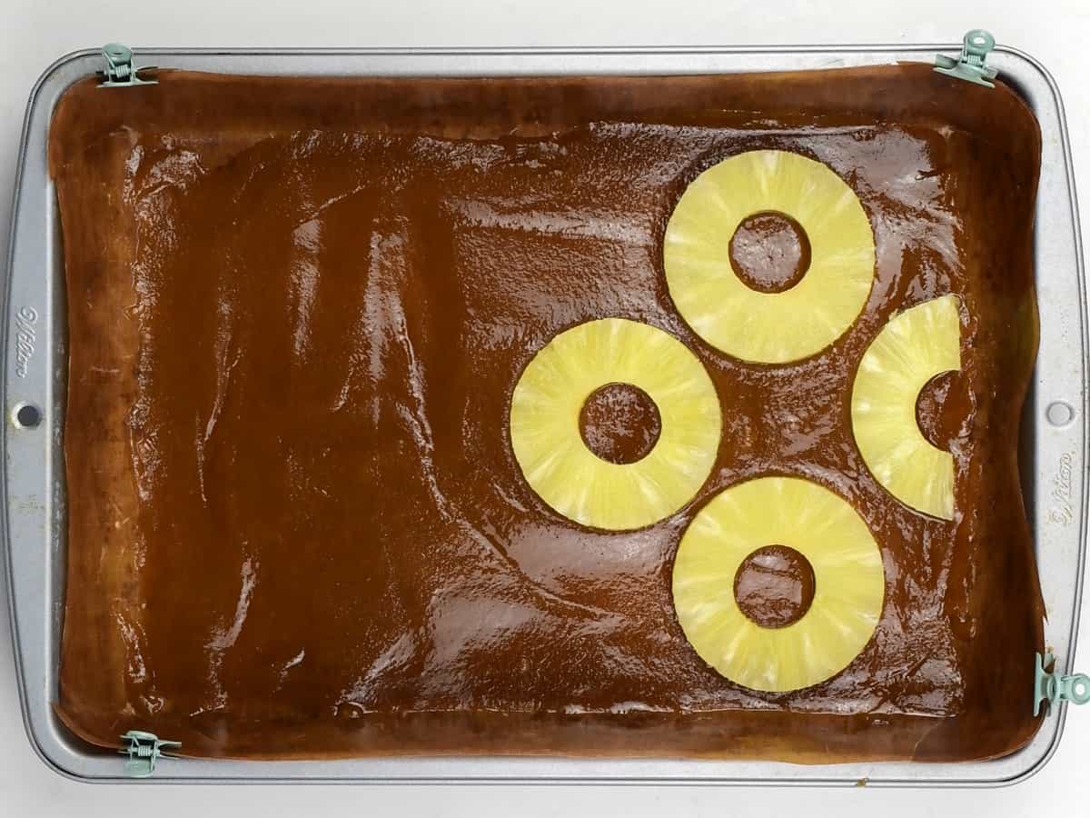 placing pineapple rings over caramel in a rectangular cake tin