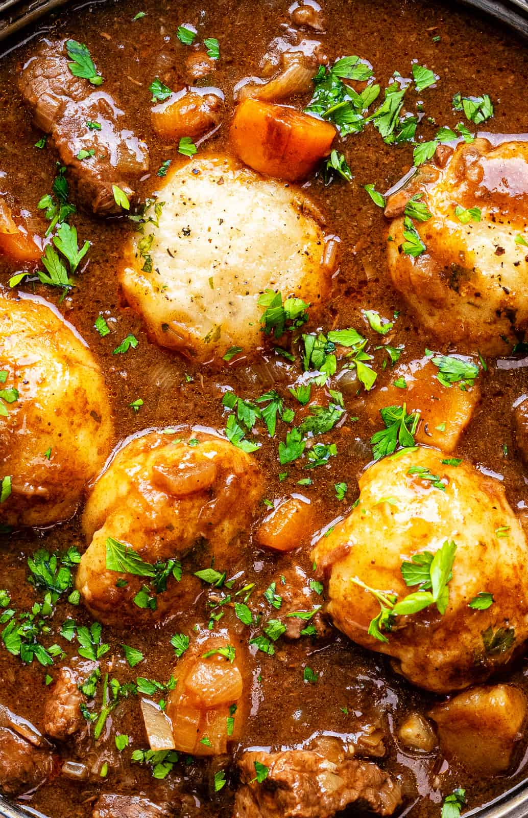 Close up on slow cooker beef casserole with dumplings garnished with fresh parsley