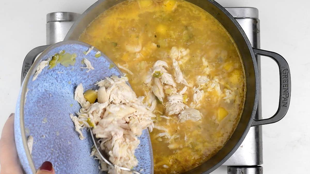 Adding shredded chicken to soup in a pot