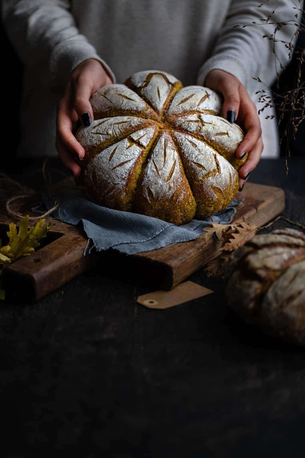 Hands holding a pumpkin shaped sourdough bread with pumpkin purée and spices