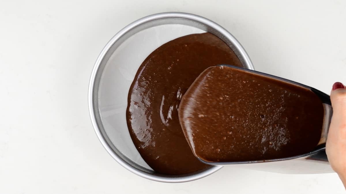 pouring chocolate cake batter into a cake tin