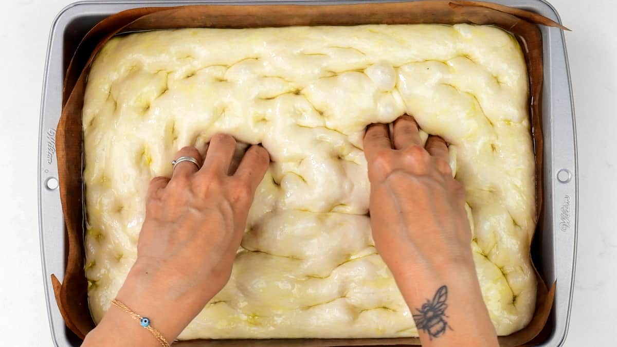 pressing fingers into sourdough focaccia dough to dimple