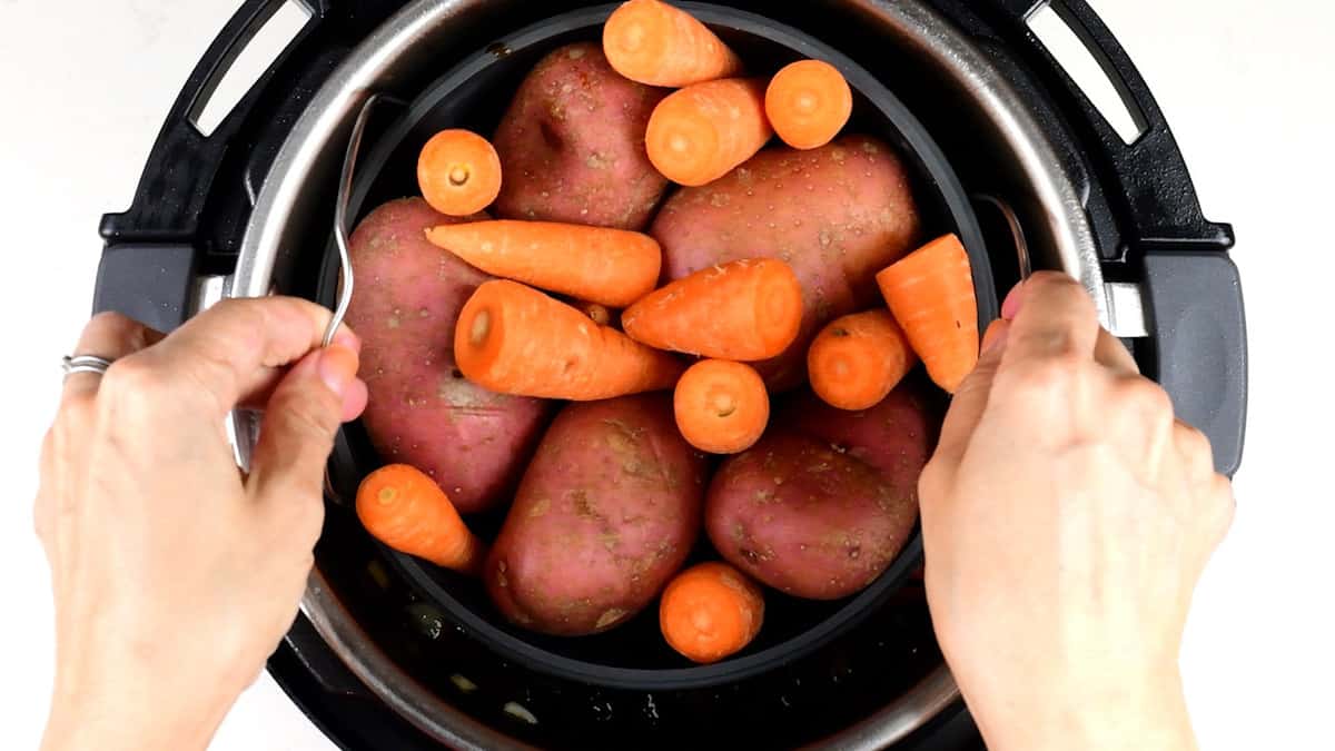 adding potatoes and carrots in a steamer into pressure cooker