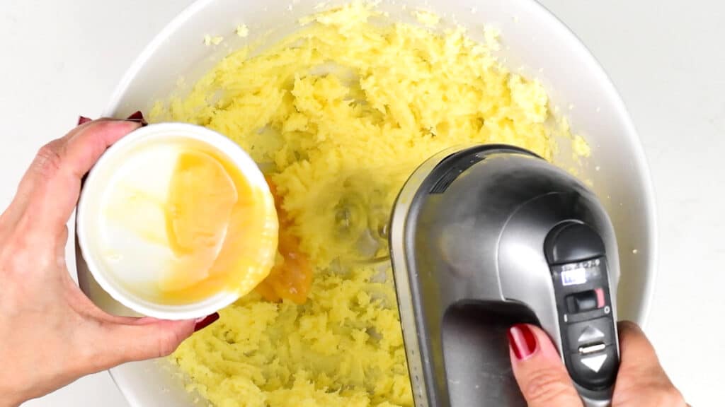 adding an egg into a mixing bowl of creamed butter and sugar