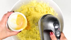 adding an egg into a mixing bowl of creamed butter and sugar