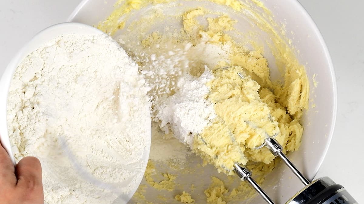 adding flour to butter and sugar in a bowl
