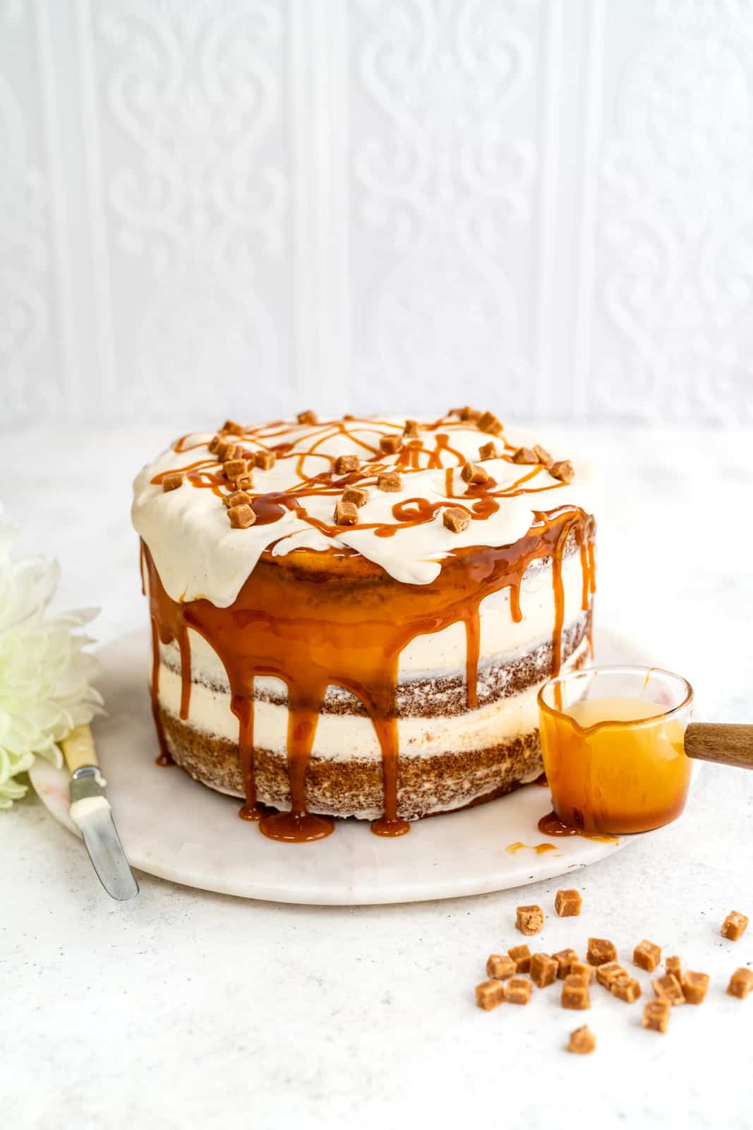 Banana Layer Cake with caramel cream cheese frosting drizzled with caramel on a marble cake plate