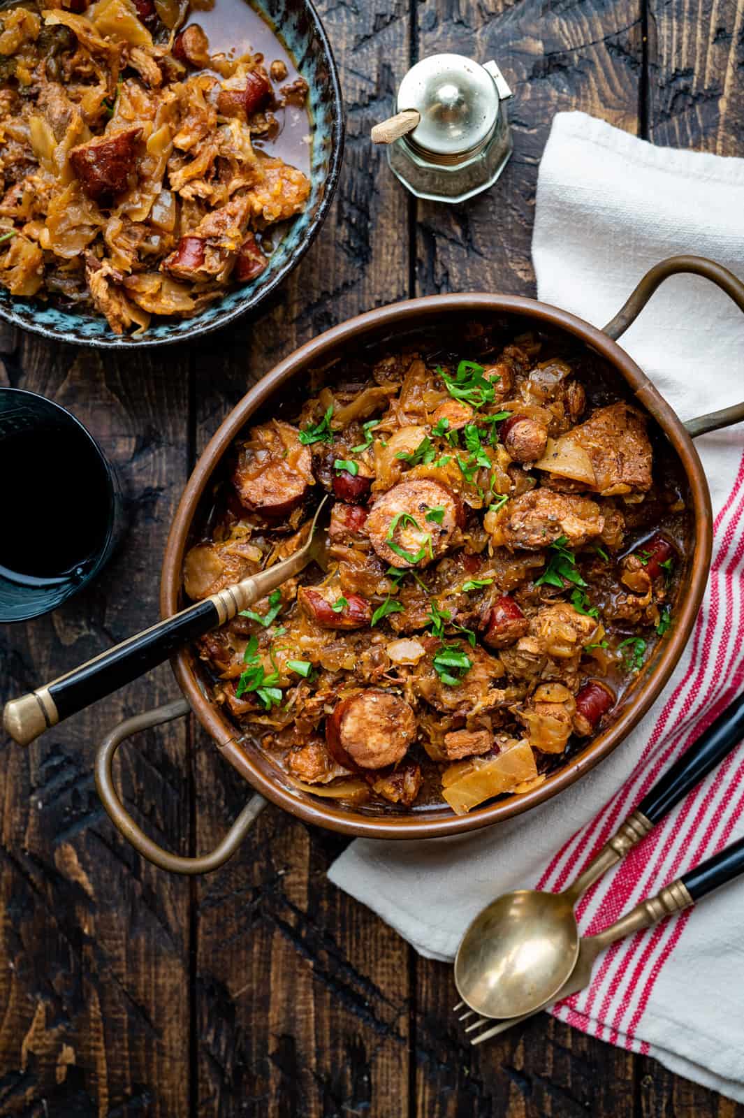 Polish bigos stew in a rustic copper casserole with a portion on the side