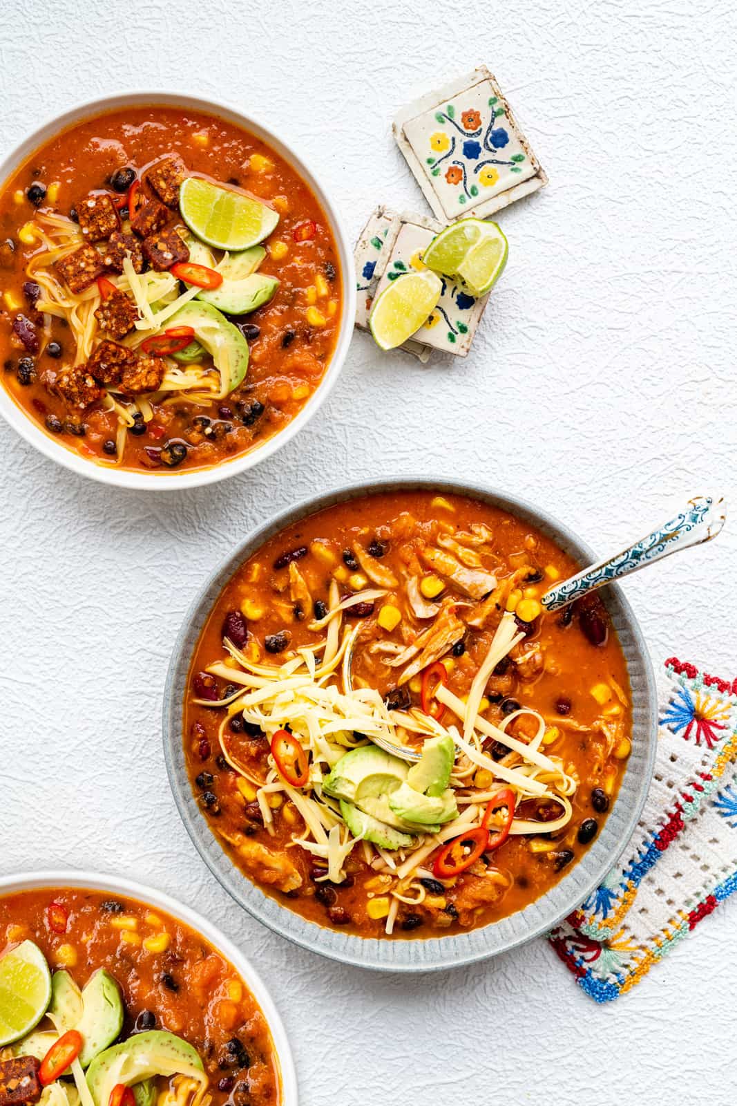 Three bowls of chicken enchilada soup topped with grated cheese, slice avocado and red chilli