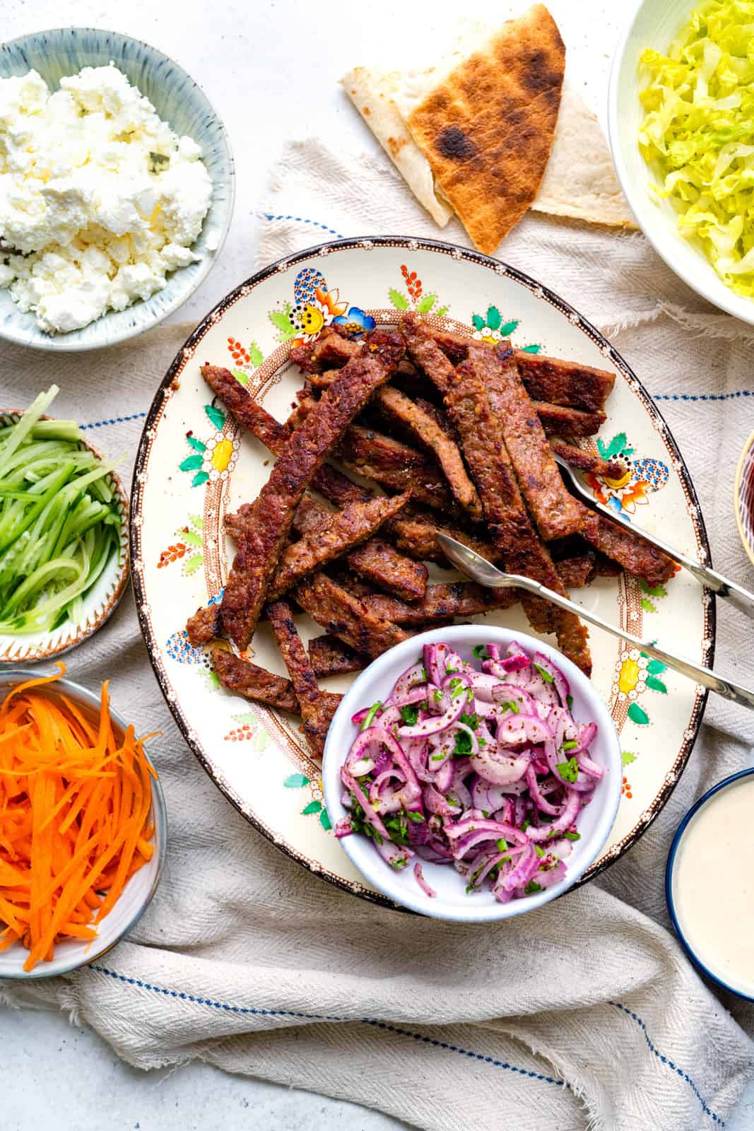 Homemade Lamb Doner meat cut into thin strips on a platter with sumac onions, lettuce and other kebab fillings