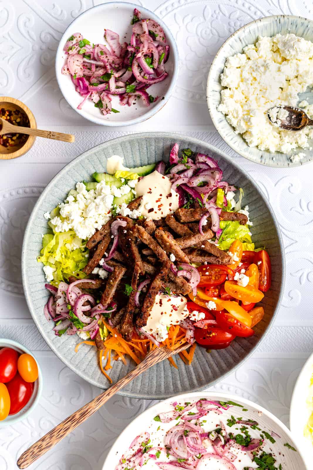 Homemade lamb doner meat cut into strips and served in a bowl with salad, sauce and feta cheese