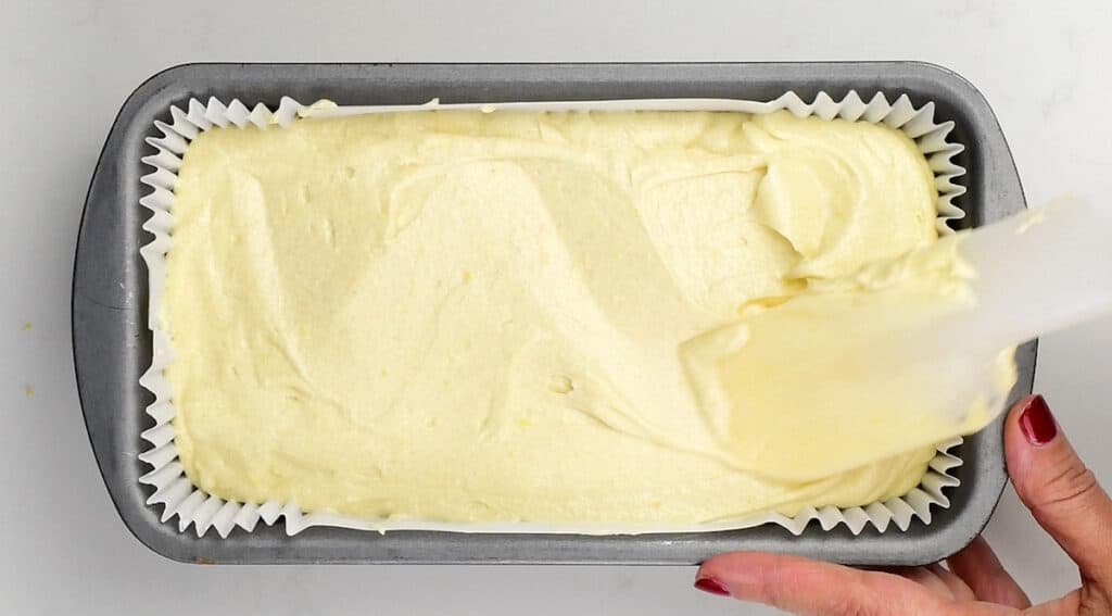 levelling vanilla cake batter in a loaf tin using a spatula
