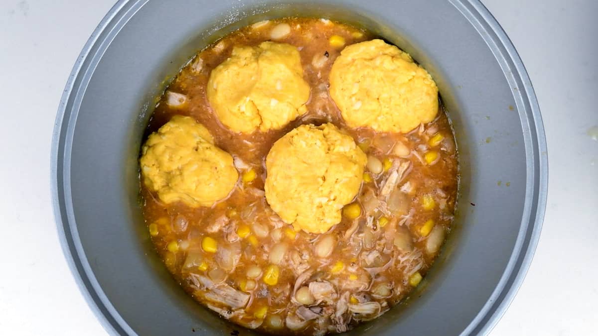 white chicken chili in a slow cooker topped with uncooked cornbread dumplings