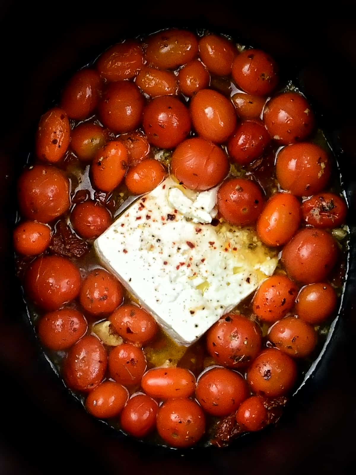 Tomatoes and block of feta cheese cooking in a slow cooker