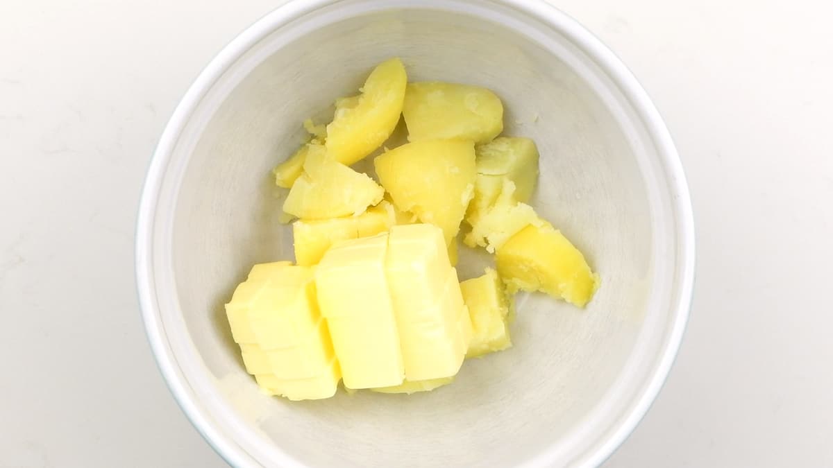 Bowl containing cubed cooked potatoes and butter