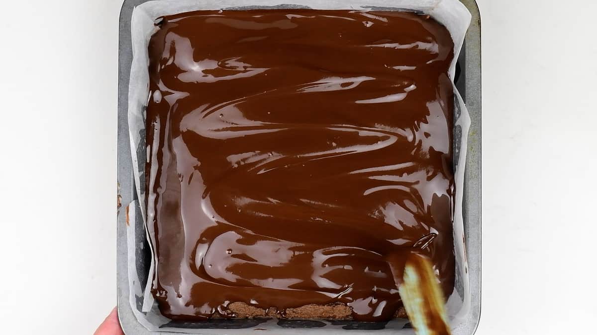 Spreading melted chocolate over tin of fudge
