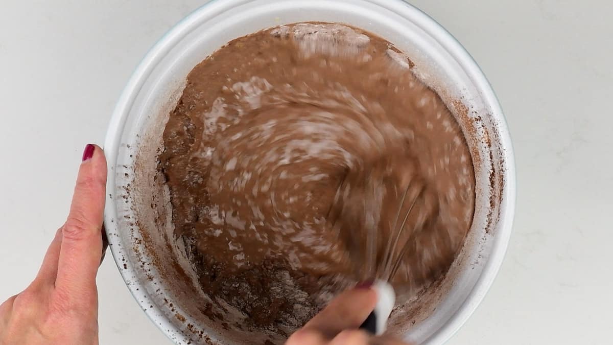 mixing chocolate pancake batter in a bowl with a balloon whisk