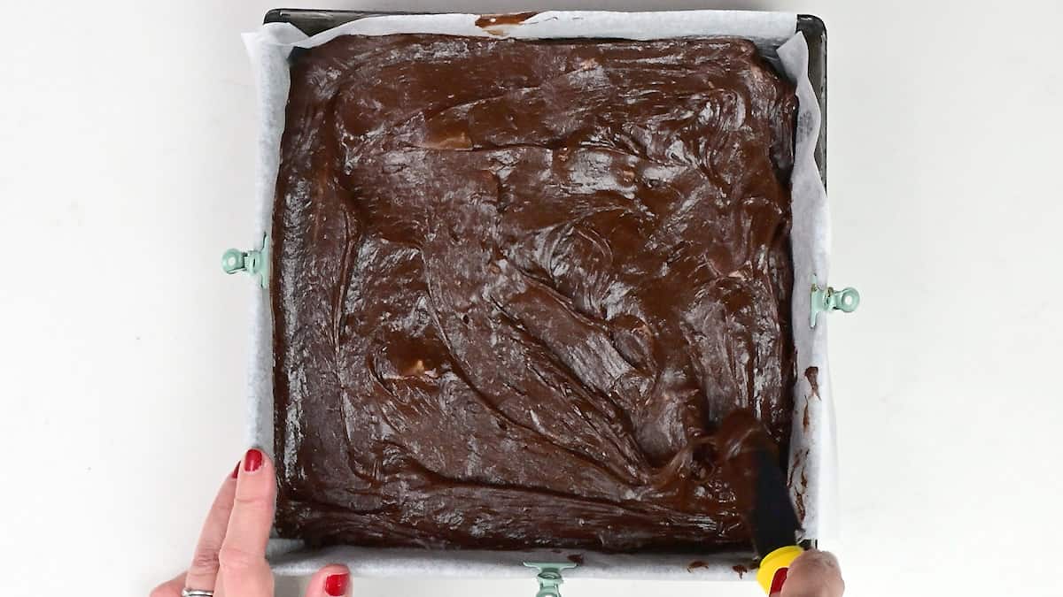 spreading brownie batter into a lined brownie pan