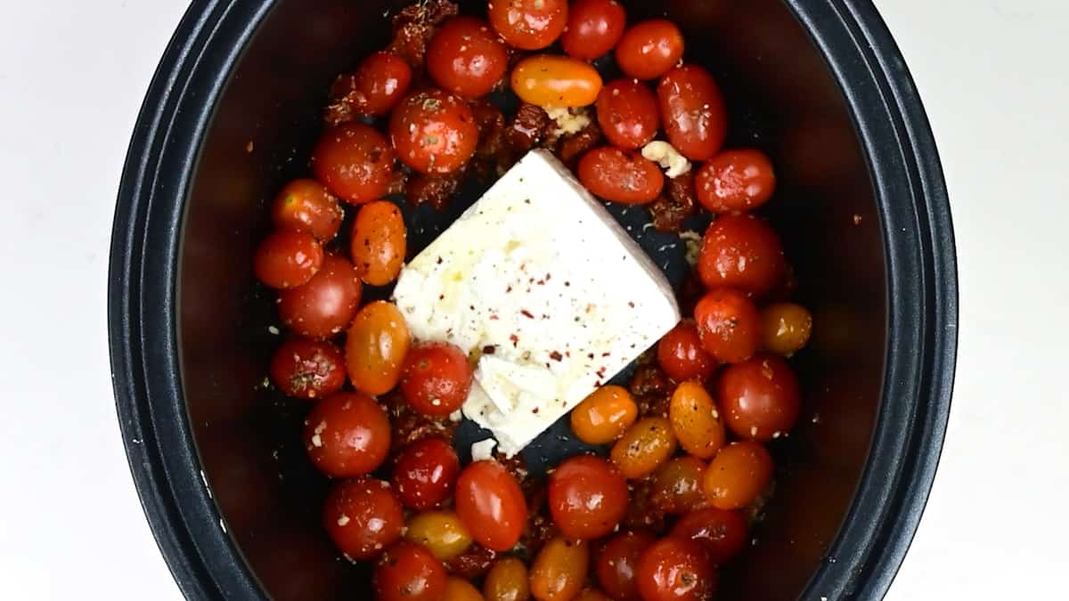 Cherry tomatoes with garlic, herbs and seasoning  and block of feta cheese in a slow cooker
