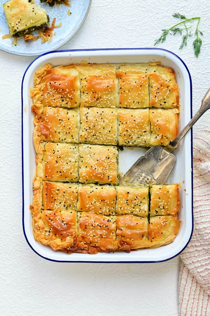 Spanakopita sliced into squares in a roasting tin with slice taken out