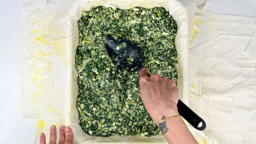 Adding spinach pie filling over filo pastry