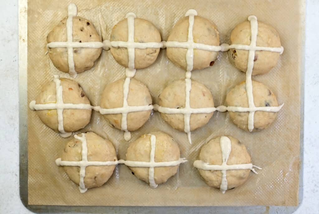 Overhead view of hot cross buns on a baking sheet with crosses piped over the top