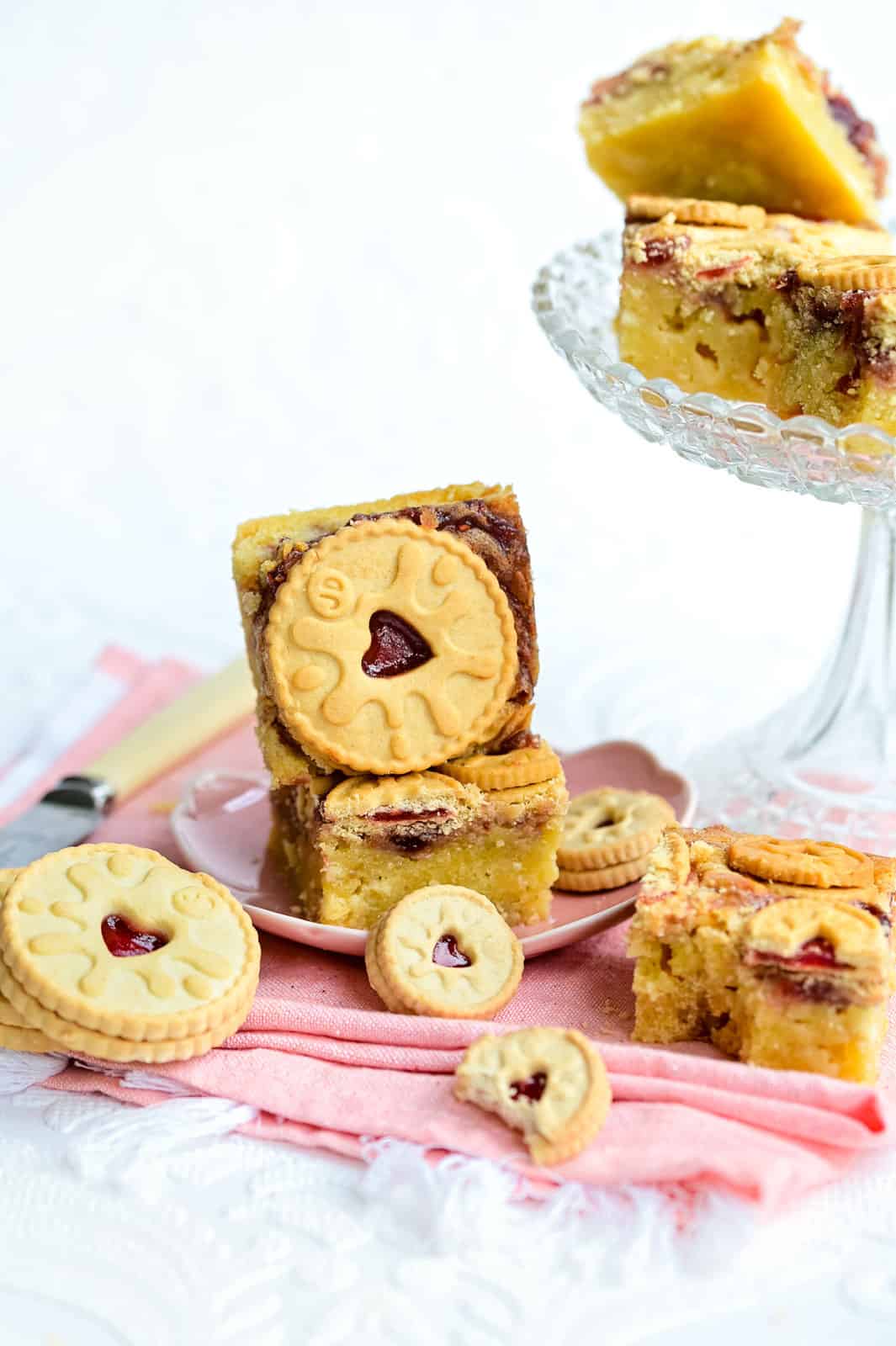 Gooey white chocolate blondies topped with Jammie Dodger biscuits on a plate and cake stand