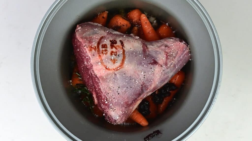 Large lamb shank in a slow cooker over a bed of vegetables