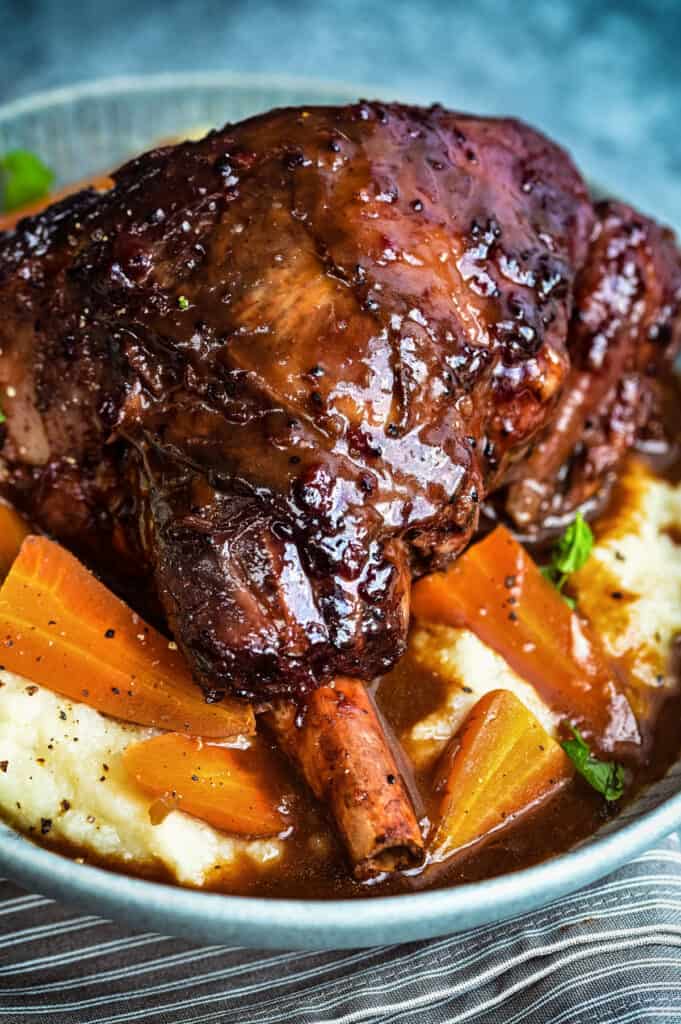 Close up on lamb shank served over mashed potatoes and carrots